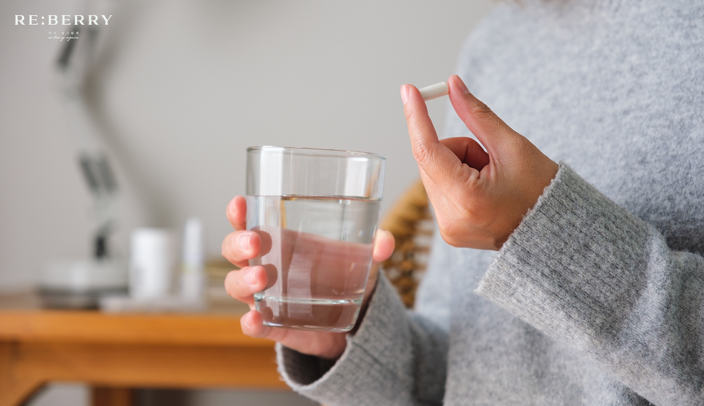 A woman holding a supplement capsule and a glass of water
