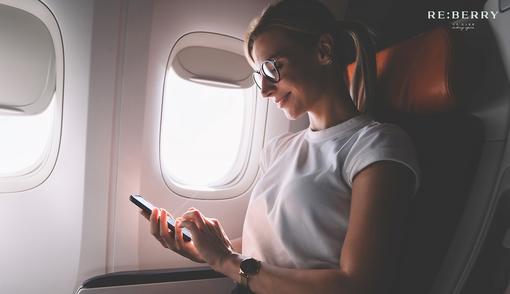 a girl sitting inside an airplane near window, using mobile