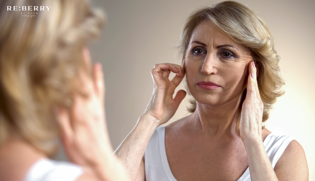 a women in her 60s with wrinkles looking at her face in mirror 